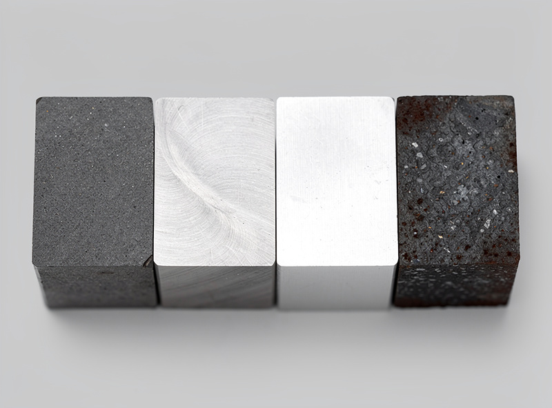 Four metal cross-section samples side by side showing color differences between mild steel, stainless steel, aluminum, and cast iron