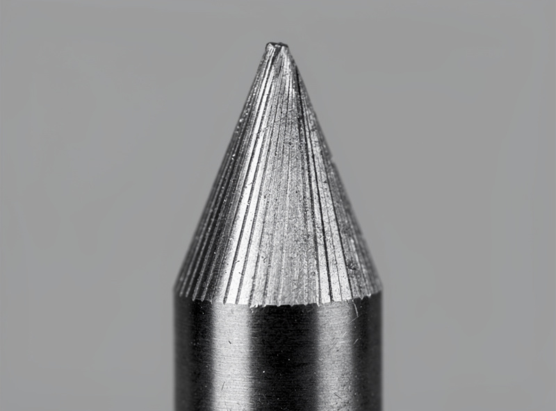 Macro photograph of a sharpened tungsten electrode tip showing the conical point with longitudinal grinding marks from a sharpening wheel