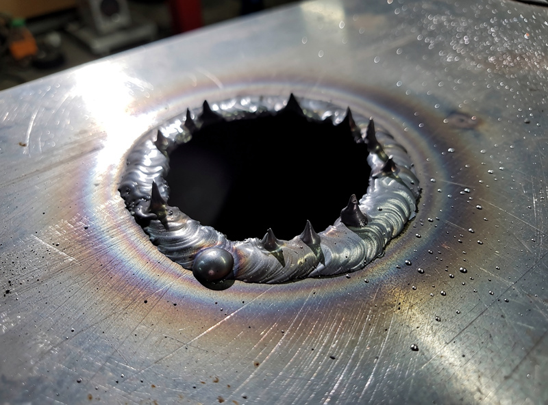 Burn-through hole in thin steel plate from excessive welding heat showing ragged melted edge