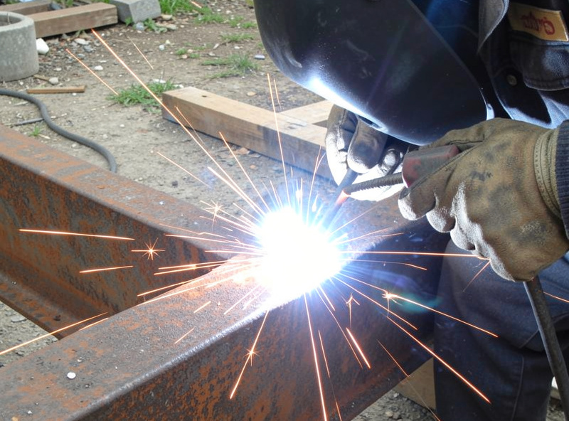 Welder striking a stick electrode arc on rusty outdoor steel with bright arc flash