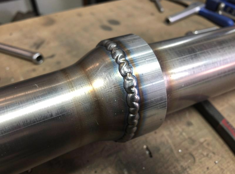 Finished welded exhaust pipe joint with a continuous ring of overlapping tack welds