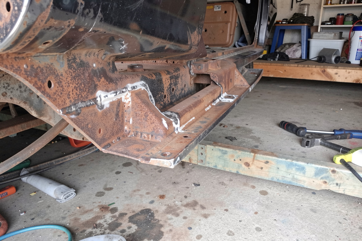 Rusty car rocker and floor area being repaired with patch panels in a home garage