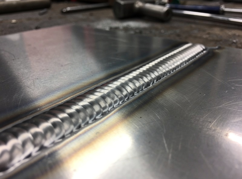 Finished stainless TIG weld bead showing light straw heat tint and clean stacked ripples on a polished panel