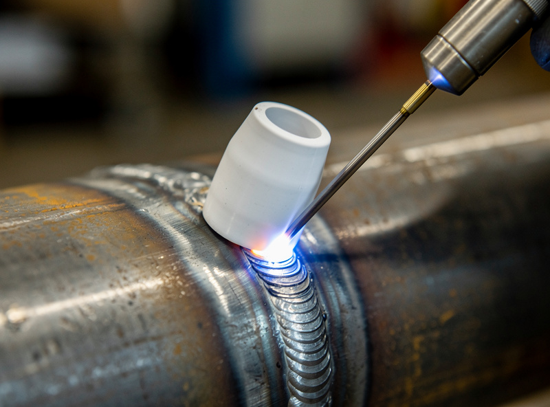 Walking the cup TIG technique on a beveled pipe joint, ceramic cup resting in the groove with stacked-dime ripples behind it