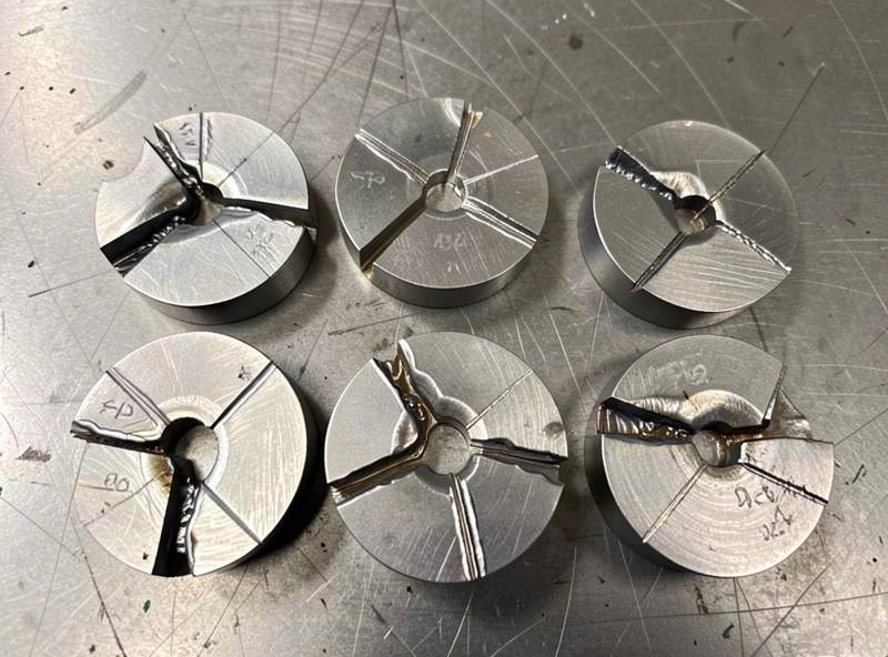 Etched weld cross sections on a steel table showing weld penetration profiles
