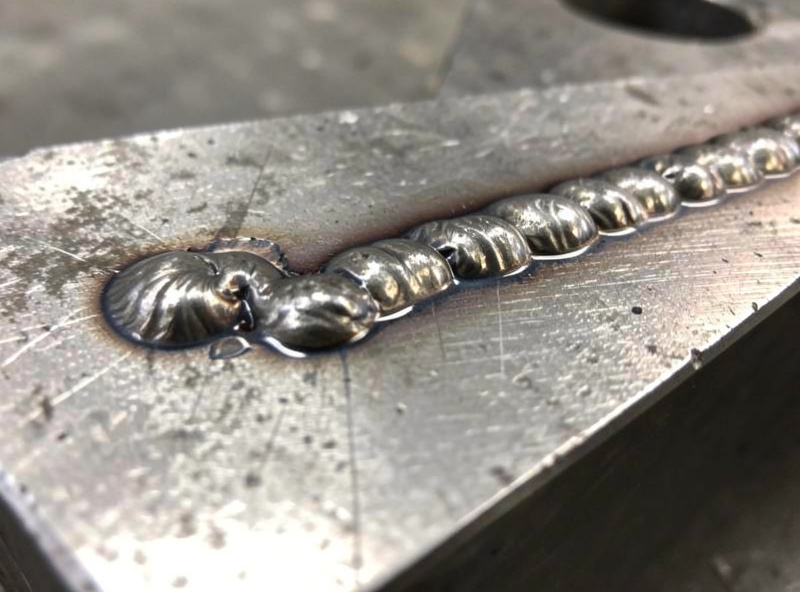 Test coupons of steel showing flux-core weld beads at different voltage settings, cold to hot