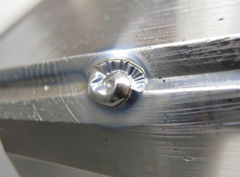 Clean steel bead after spatter has been wire-brushed and ground away, bright metal around the weld