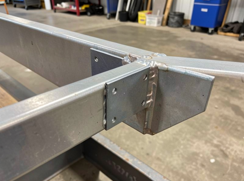 Square steel stake pockets welded at intervals along the side rail of a utility trailer