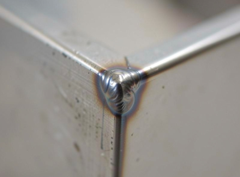 Macro close-up of a fully welded corner joint on 2x3 inch rectangular steel tube with a clean MIG bead