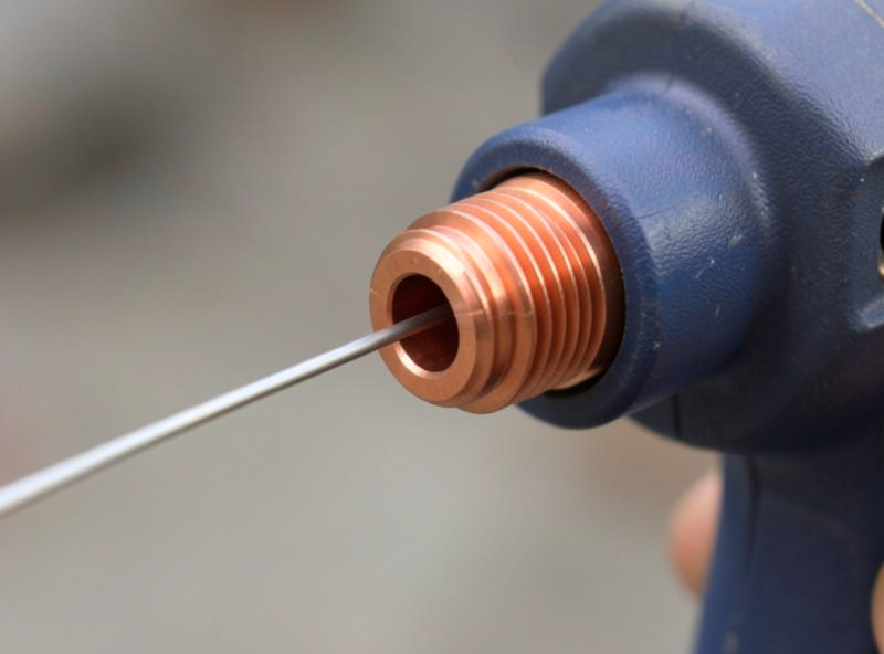 Close-up of a copper contact tip threaded into a MIG gun with welding wire feeding through the bore