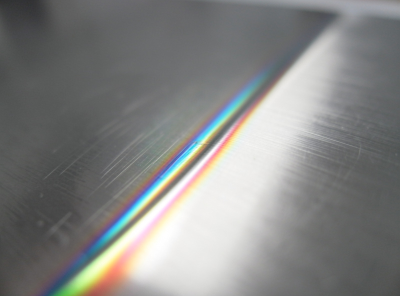 Close-up of a stainless steel weld bead showing rainbow heat-tint colors along a stainless plate