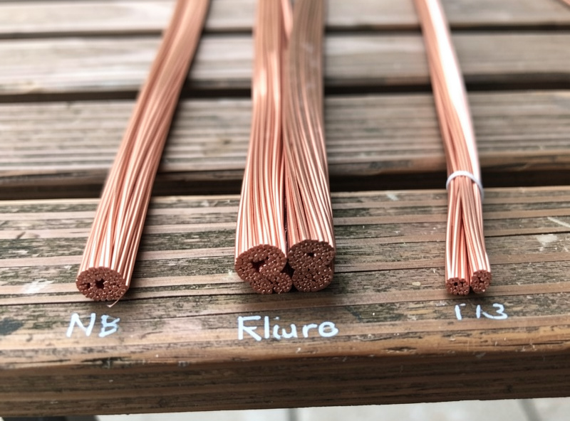 Three thicknesses of copper electrical wire compared side by side on a wooden bench